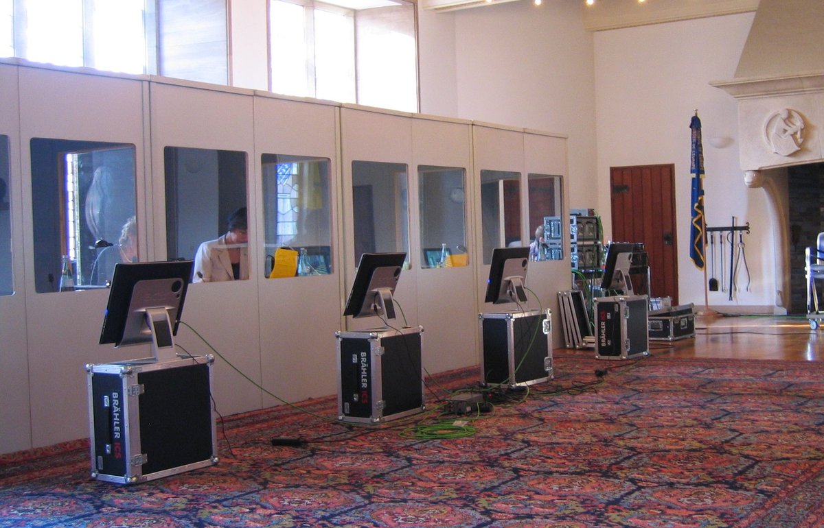 Mehrere Dolmetscherkabinen mit Monitoren für die Dolmetscher, auf denen die Präsentationen und Redner per Video übertragen werden.